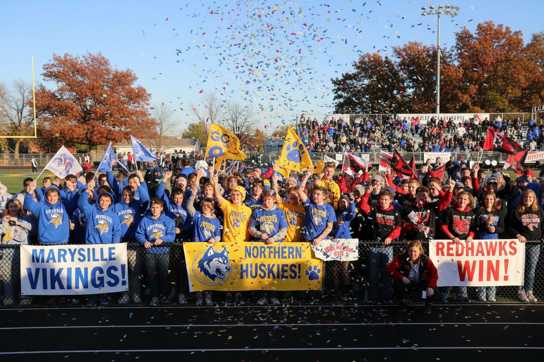 Students and fans cheering at a Michigan high school pep rally wearing custom spirit wear in Marysville Vikings blue and white, Northern Huskies yellow and blue, and Port Huron Redhawks black red