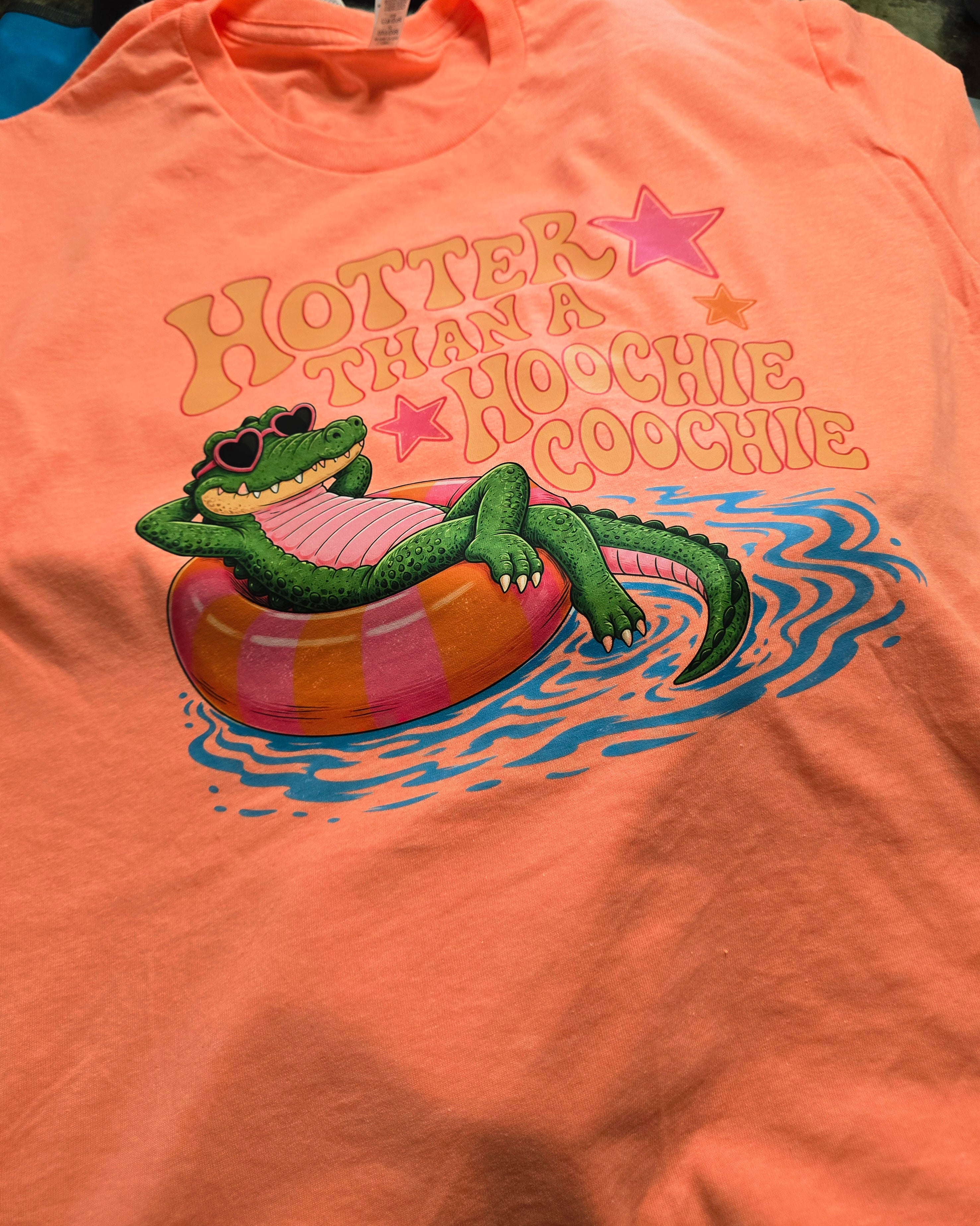 Orange t-shirt with a graphic of a crocodile on an inner tube and text 'Hotter than a hoochie coochie'.