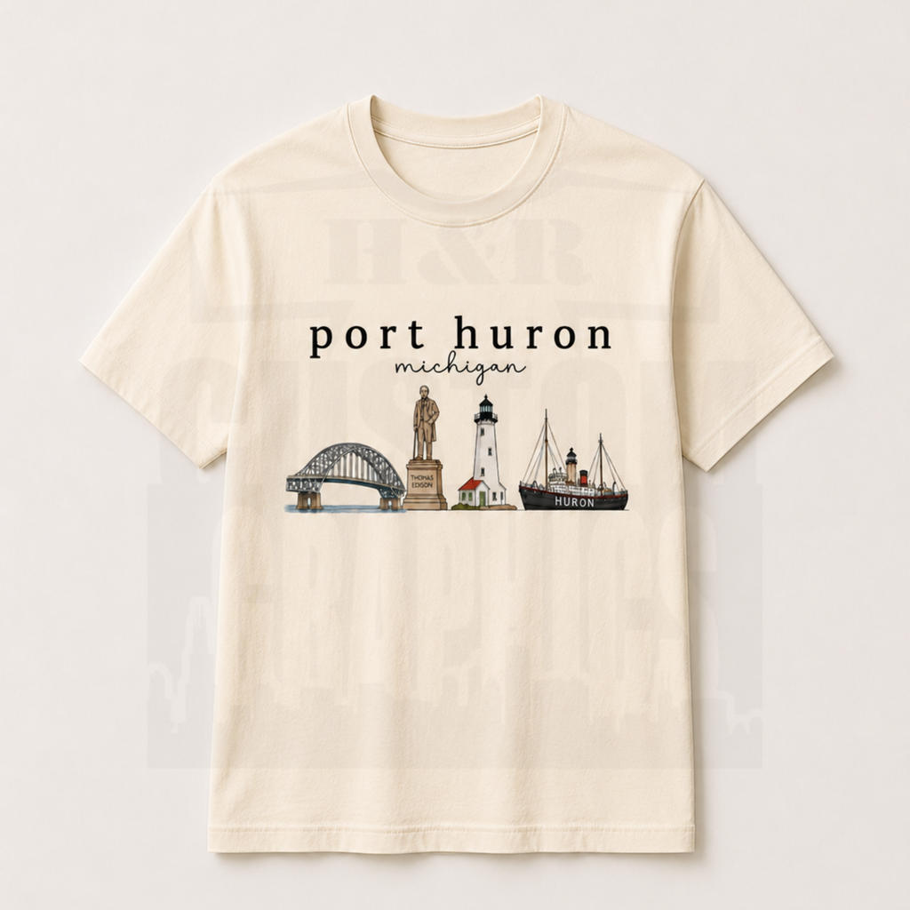 An off-white short-sleeve crewneck t-shirt featuring a graphic print of Port Huron, Michigan landmarks including the bridge, lighthouse, and ship, displayed on a light beige background.