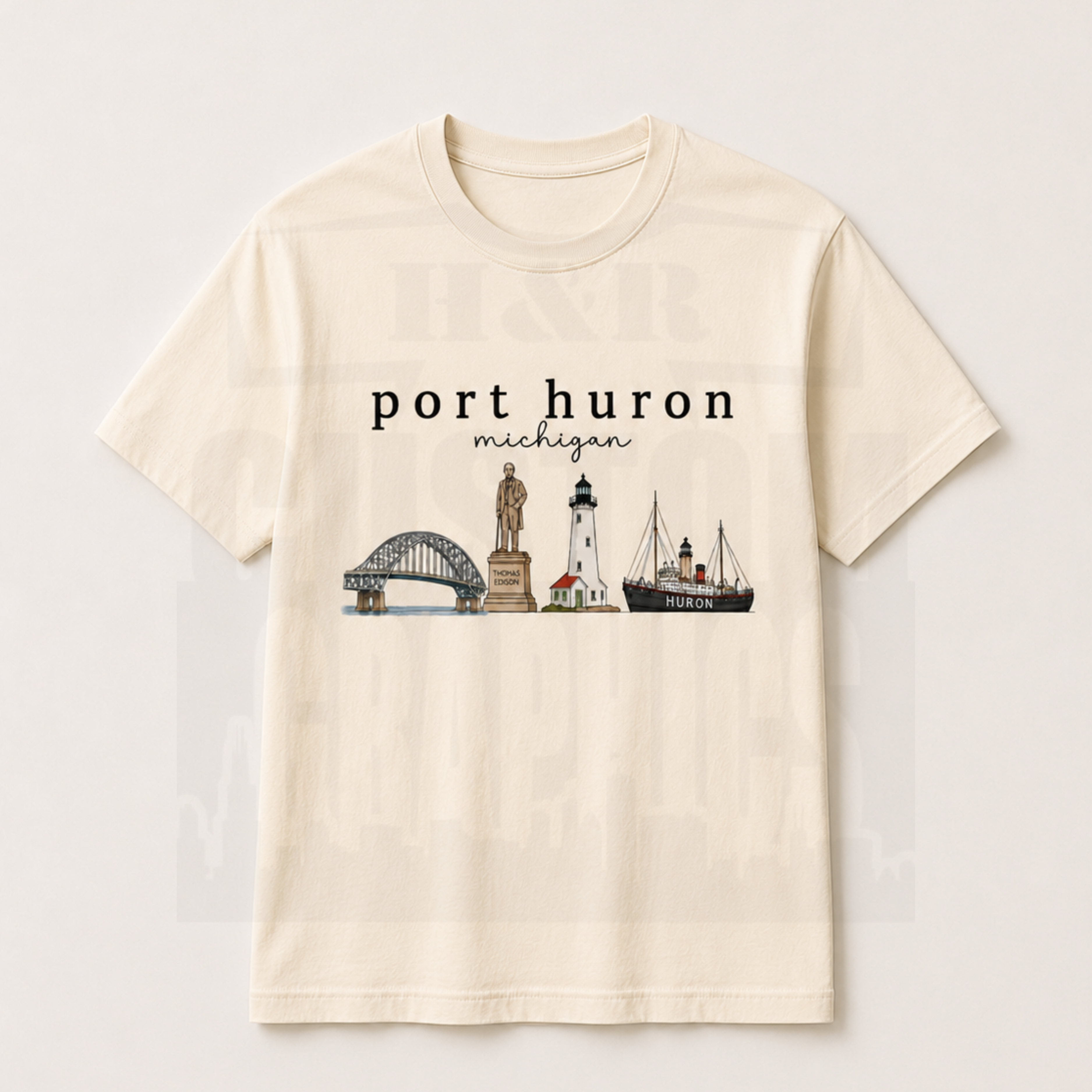 An off-white short-sleeve crewneck t-shirt featuring a graphic print of Port Huron, Michigan landmarks including the bridge, lighthouse, and ship, displayed on a light beige background.