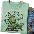 Light green t-shirt with a graphic of a frog riding a turtle and text, next to jeans and keys.