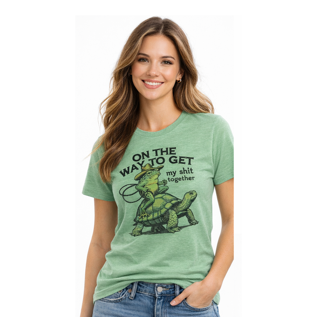 Light green t-shirt with a graphic of a frog riding a turtle and text, next to jeans and keys.