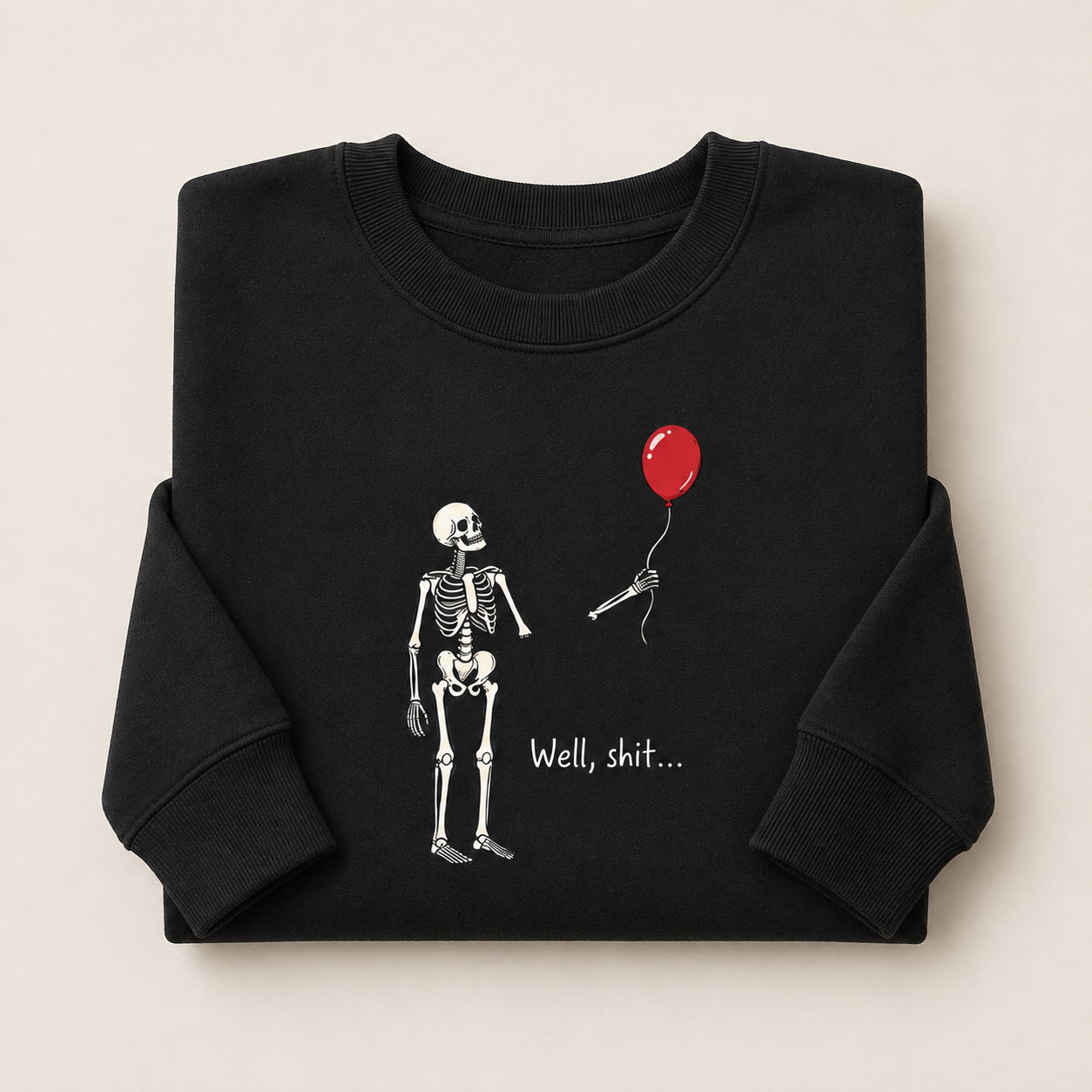 A folded black crewneck sweatshirt on a light beige background, featuring a graphic of a white skeleton holding a red balloon with the text 'Well, shit.